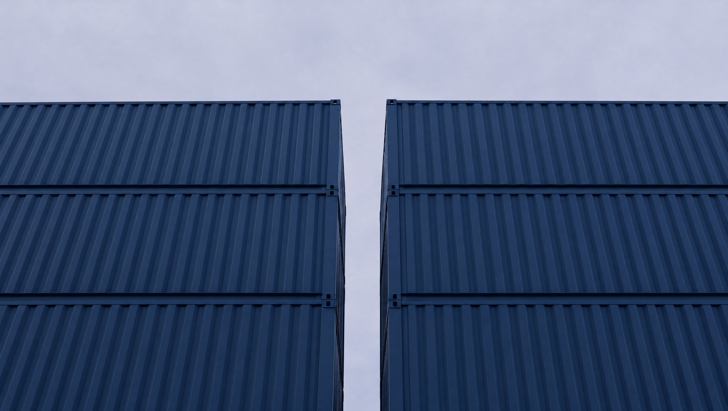 Stacked navy shipping containers against a pale sky